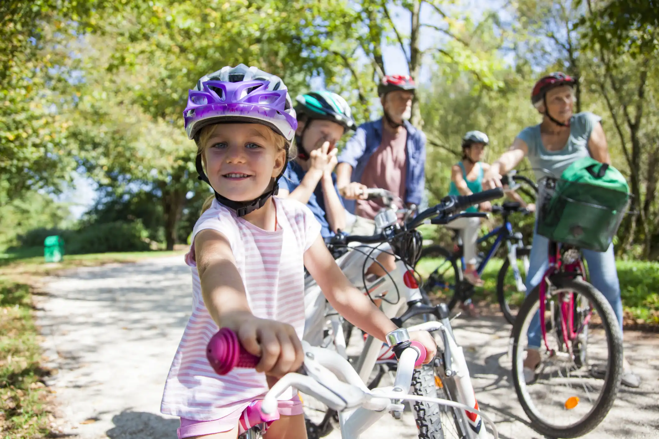 Family riding bicycles together on a sunny path in a park.